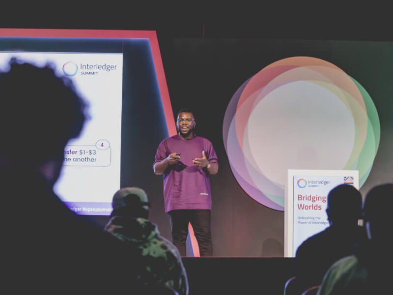 Uchi Uchebeke presenting on stage at Interledger Summit, with audience silhouettes in the foreground.
